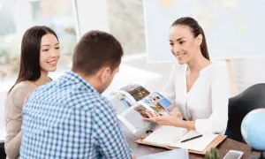 Pracownica biura podróży pokazuje klientom katalog z ofertami wakacyjnymi.