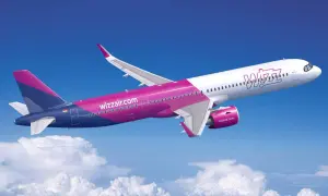 Samolot Wizz Air w locie na tle błękitnego nieba z chmurami.