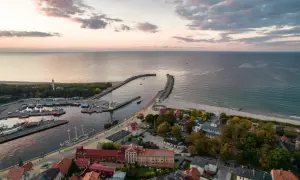 Widok z lotu ptaka na port w Ustce z łodziami, latarnią morską i plażą o zachodzie słońca.