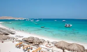 Plaża z białym piaskiem, turkusową wodą, łodziami i parasolami.