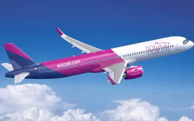 Samolot Wizz Air w locie na tle błękitnego nieba z chmurami.