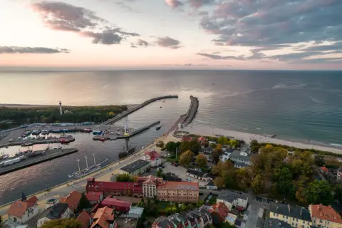 Widok z lotu ptaka na port w Ustce z łodziami, latarnią morską i plażą o zachodzie słońca.