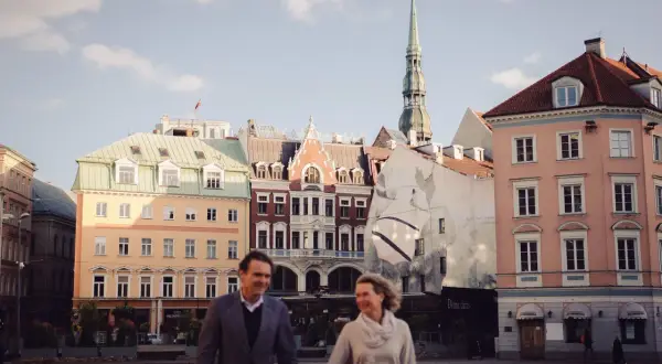 Para spaceruje po Rynku w Rydze, w tle zabytkowe kamienice i wieża kościelna.
