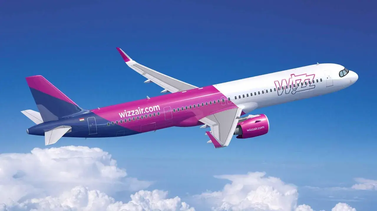 Samolot Wizz Air w locie na tle błękitnego nieba z chmurami.