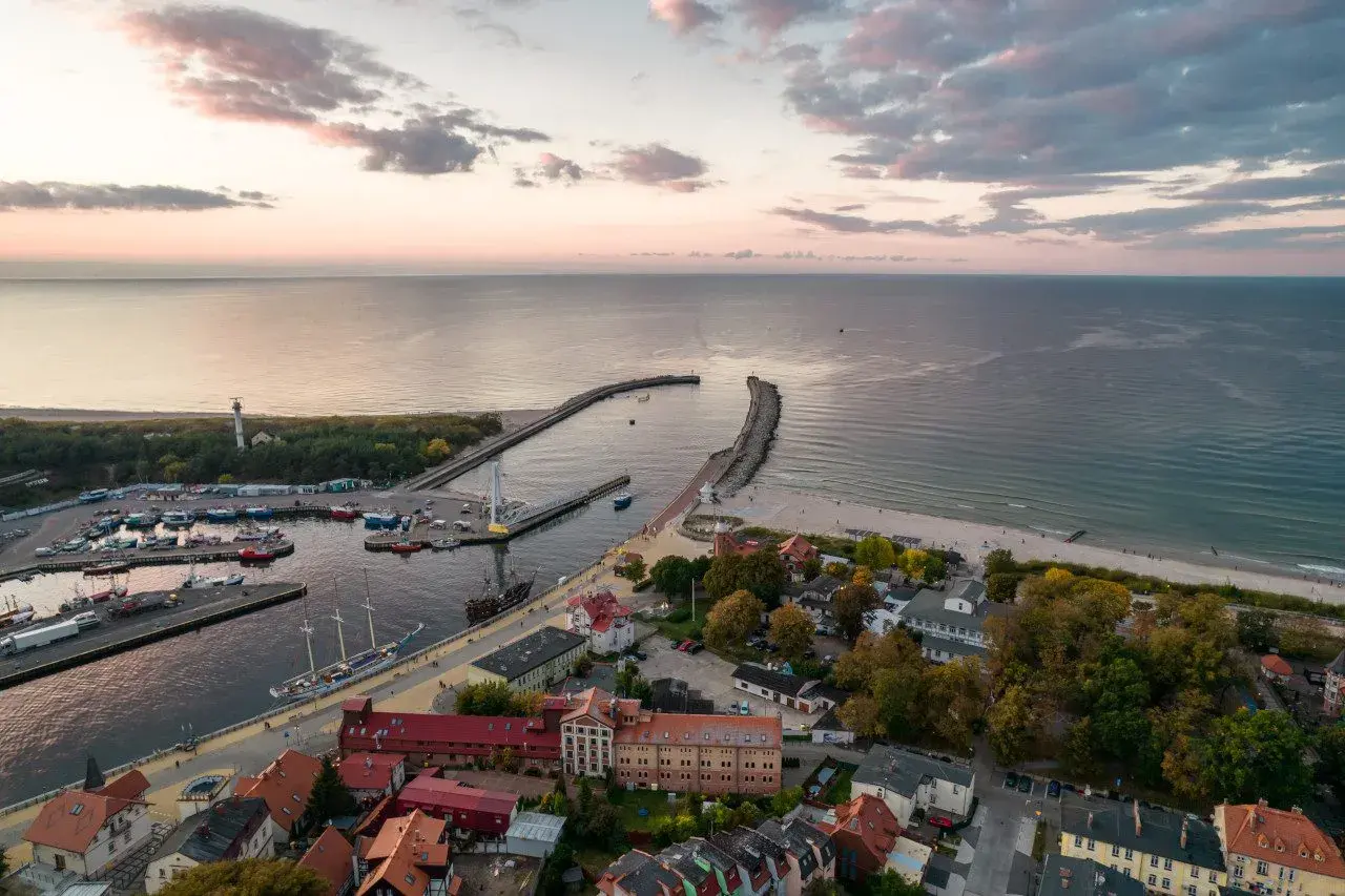 Widok z lotu ptaka na port w Ustce z łodziami, latarnią morską i plażą o zachodzie słońca.