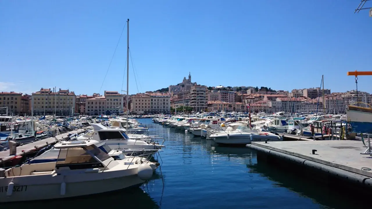 Widok na port w Marsylii z wieloma łodziami i budynkami w tle.