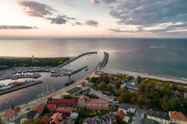 Widok z lotu ptaka na port w Ustce z łodziami, latarnią morską i plażą o zachodzie słońca.