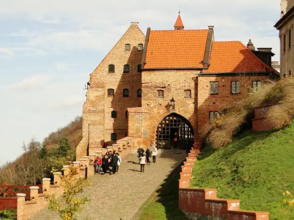 Zamek w Grudziądzu z bramą i grupą turystów na brukowanej ścieżce.
